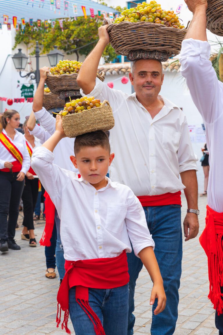 Un niño y varios adultos llevando una cesta con uvas en la procesión de la Fiesta de Viñeros de Moclinejo