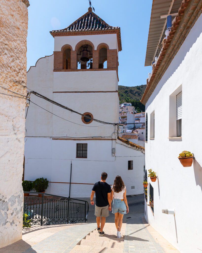 Calle de Moclinejo con vistas a la iglesia y una pareja joven andando