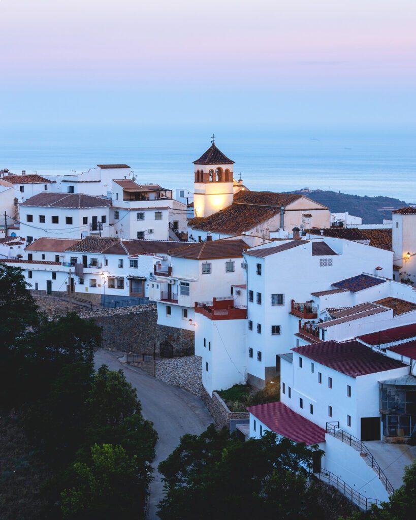 Vista de Moclinejo al anochecer con la iglesia iluminada y el mar de fondo