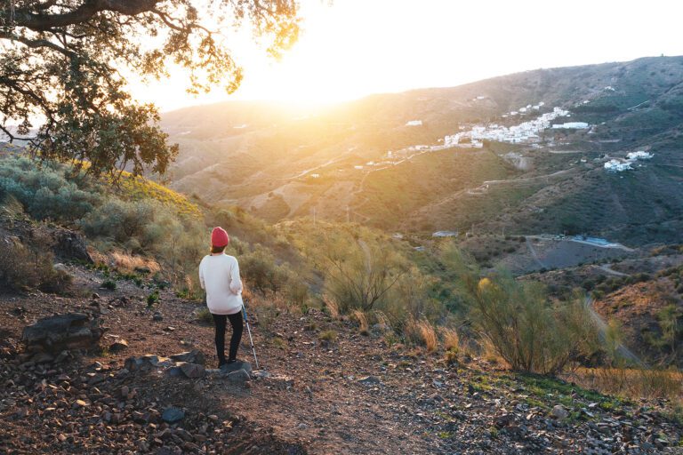 Mujer senderista mirando hacia Moclinejo desde una ruta de senderismo al atardecer